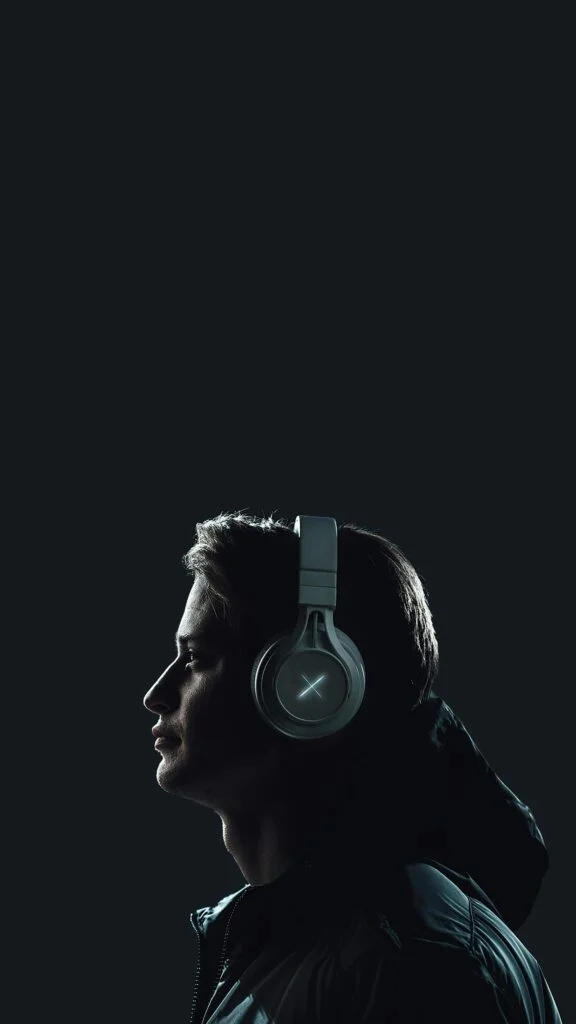 Moody portrait of a young man wearing headphones against a dark studio backdrop.